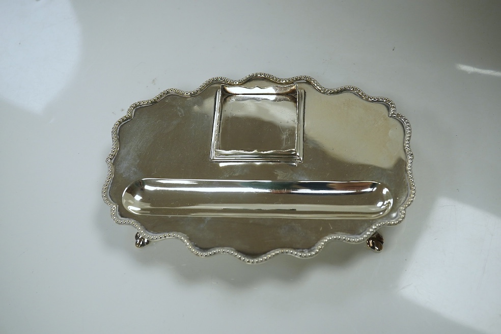 An Edwardian silver shaped oval inkstand, with wavy border, silver mounted glass well and pen recess, Skinner & Co, London, 1908, 15.8cm, together with a later engine turned silver cigarette case, 10.6oz. Condition - fai